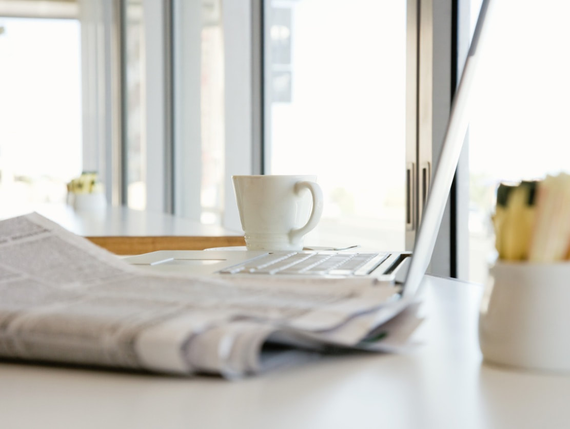 folded newspaper next to open laptop and cup of coffee